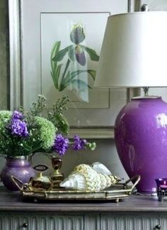 a purple vase sitting on top of a table next to a lamp and other items