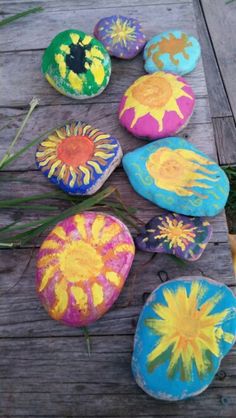 colorful painted rocks sitting on top of a wooden deck next to grass and flowers in the middle