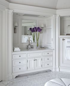 a bathroom with white cabinets and purple flowers