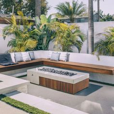 an outdoor fire pit surrounded by palm trees and seating on concrete slabs with benches in the foreground