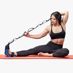 a woman sitting on a yoga mat with a resistance band attached to her back and holding onto the straps