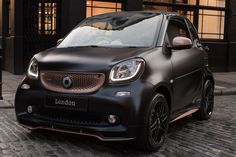 a black smart car parked in front of a building on a cobblestone street