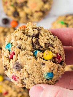 a hand holding a cookie with m & m cookies in the background