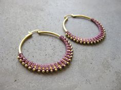 a pair of gold and purple beaded hoop earrings sitting on top of a cement surface