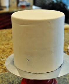 a white frosted cake sitting on top of a red stand in front of a counter