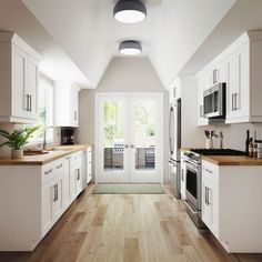 an open kitchen with white cabinets and wood flooring on the walls, along with large windows