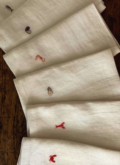 six pieces of white linen with red embroidered designs on them, sitting on a wooden table