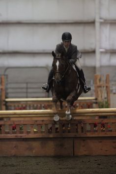 a man riding on the back of a brown horse over an obstacle in a barn