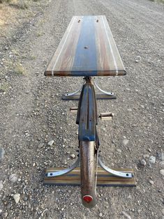 a wooden table sitting on the back of a bike in the middle of gravel road