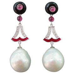 A pair of art deco style earrings, with an upper part consisting of 2 black onyx buttons with in the center 2 small round ruby cabochons, a central part where we have 2 elements in white gold, diamonds and red enamel,that support 2 white baroque pearls of 13 mm in diameter In 1978 our workshop started in Italy to make simple-chic Art Deco style jewellery, completely handmade and using the typical gemstones of that period (1920-1930 circa) : genuine Jades, Turquoise , Coral, Lapis Lazuli and othe Art Deco Ruby Earrings, Luxury Classic Ruby Earrings, Red Oval Art Deco Jewelry, Luxury Red Earrings With Gemstone Accents, Red Ruby Earrings With Intricate Design, Black Onyx Earrings, Chic Art, Gold Pearl Earrings