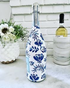 a blue and white bottle sitting on top of a counter next to a vase with flowers