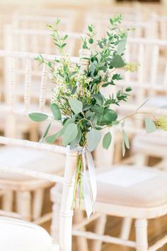 a bouquet of greenery is tied to the back of a chair at a wedding