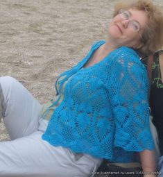 a woman laying on the ground wearing a blue crocheted shawl and glasses