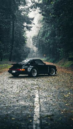 a black sports car parked on the side of a road in the middle of some trees