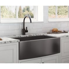 a stainless steel sink in a kitchen with marble counter tops and white cabinets, along with two windows