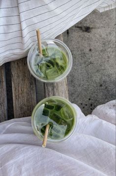 two cups filled with green tea sitting on top of a wooden chair next to a white blanket