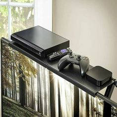 a video game console sitting on top of a table next to a window with a forest scene behind it