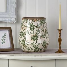 a white vase sitting on top of a dresser next to a framed picture and candle