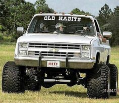 an older pickup truck is parked in the middle of a field with trees and grass behind it