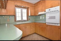 an empty kitchen with wooden cabinets and green counter tops, along with a white stove top oven