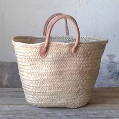 a large woven basket sitting on top of a wooden table next to a white wall