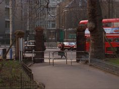 a red double decker bus driving down a street next to a park area with trees