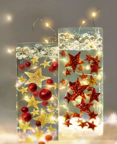 two clear vases with red and gold stars in them on a white surface surrounded by christmas lights