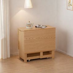 a small wooden cabinet in a room with white walls and wood flooring, next to a lamp