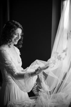 A woman in a wedding dress stands by a window, smiling as she holds a veil in her hands. The image is in black and white. Photography by Susan Stripling. Dress a custom design by Pnina Tornai. Pnina Tornai, Groom Getting Ready, Island City, Long Island City, A Wedding Dress, Summer Weddings, Outdoor Wedding Venues, Nyc Wedding