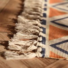 an orange, blue and white rug with fringes on it sitting on a wooden floor