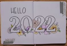 an open notebook with flowers and the words hello 202 written in it on a wooden surface