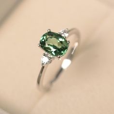 a ring with an oval cut green stone surrounded by three diamonds on a white surface