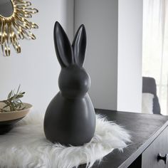 a gray rabbit statue sitting on top of a table next to a mirror and bowl