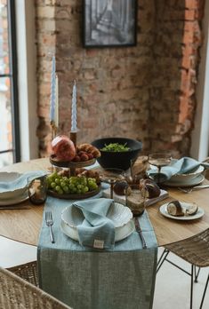 a table set with plates, silverware and fruit on it in front of a brick wall