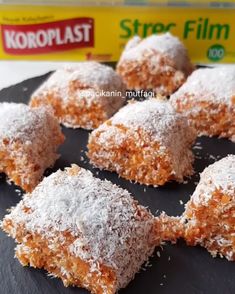 powdered sugar covered pastries on a black plate next to a box of kroplast film