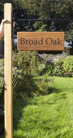 a wooden sign hanging from the side of a lush green field