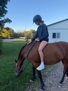 a girl riding on the back of a brown horse next to a white building and green grass