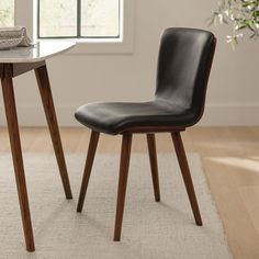 a black leather dining chair next to a white rug in front of a table with a potted plant on it