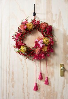 a pink wreath hanging on the wall with flowers and tassels attached to it