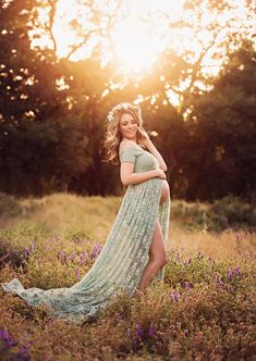 a pregnant woman standing in a field at sunset