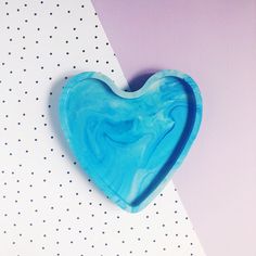 a blue heart shaped object sitting on top of a white and purple background with dots