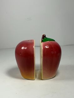 an apple shaped vase with a green leaf sticking out of it's side, sitting on a white surface