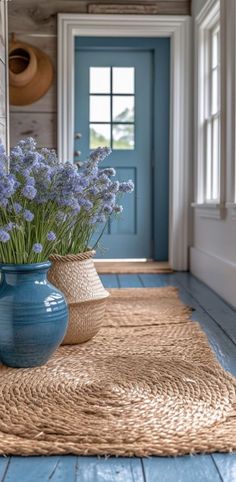 two vases filled with purple flowers sitting on top of a blue rug in front of a door