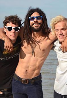 three men standing next to each other in front of the ocean with their arms around one another