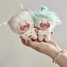 a hand holding two small stuffed animals with blue hair on top of each one's head