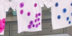 three t - shirts hanging on a clothesline with blue and pink flowers painted on them