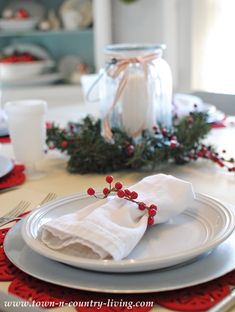 the table is set for christmas dinner with white plates and red napkins on it