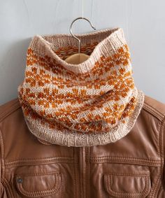 an orange and white knitted scarf hanging from a leather jacket hang on a hook