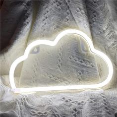 a white cloud shaped neon light sitting on top of a bed next to a blanket