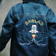 a child's denim jacket with an image of a rocket ship on it and the words barlas written in gold